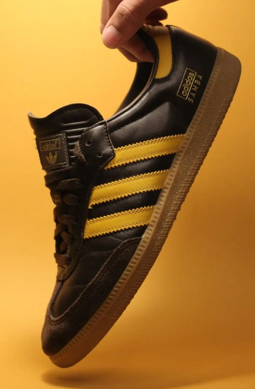 Hand holding a black and gold trainer against yellow